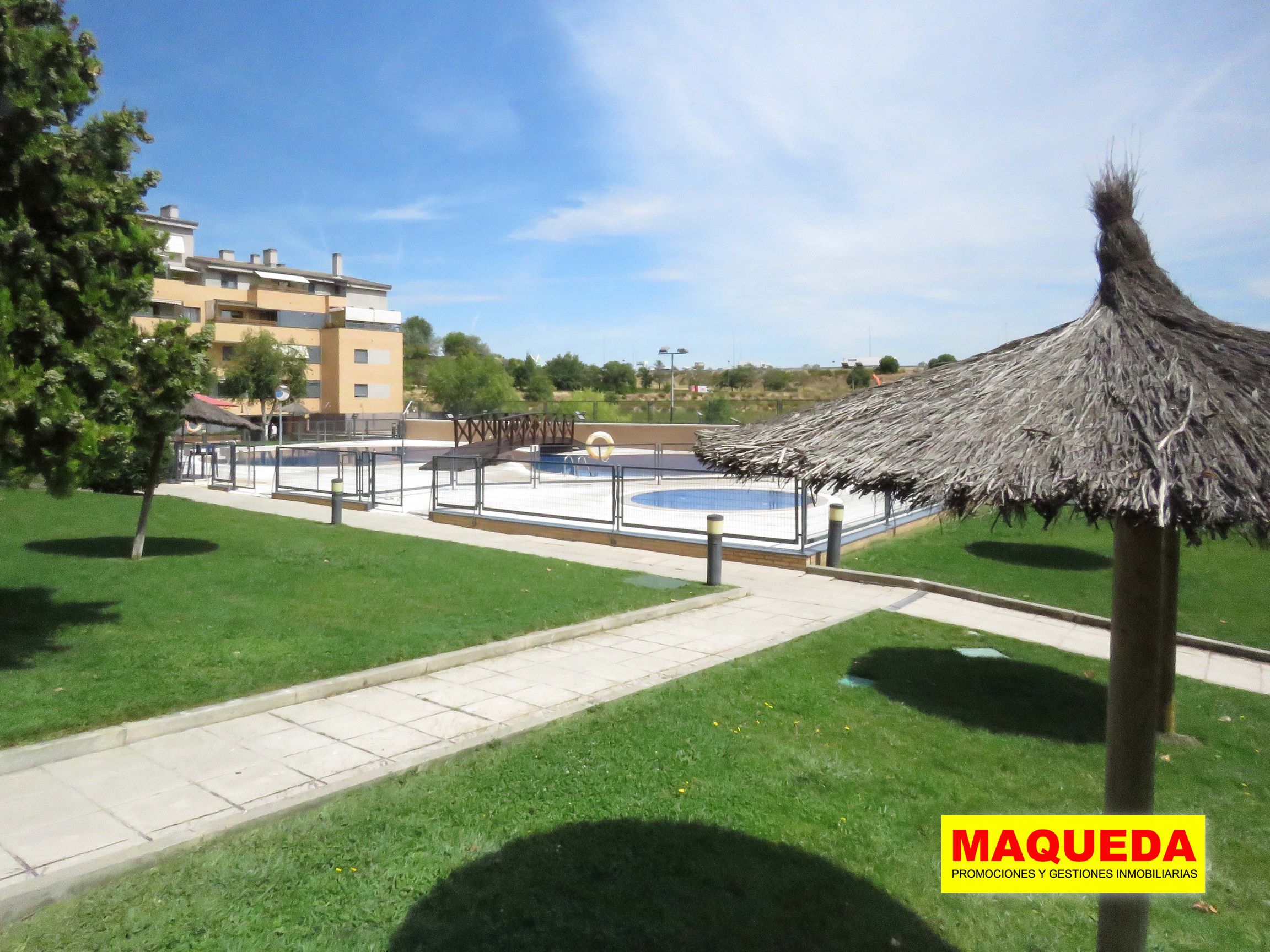 Zona de césped con sombrillas y piscinas al fondo