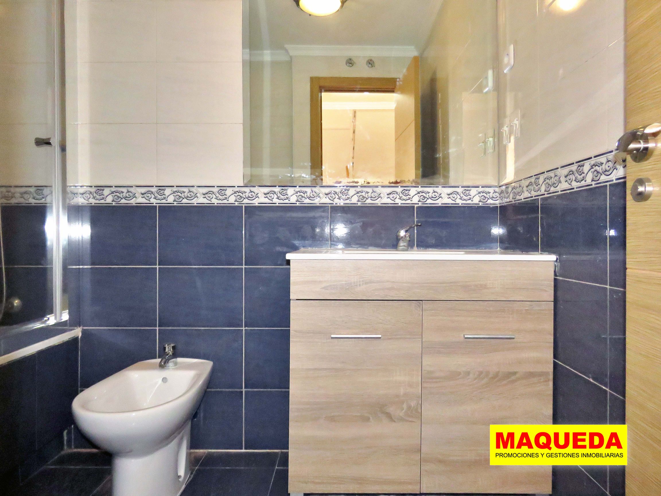 Baño completo en la planta alta con azulejos en tonos blancos y azules y mueble de lavabo en madera