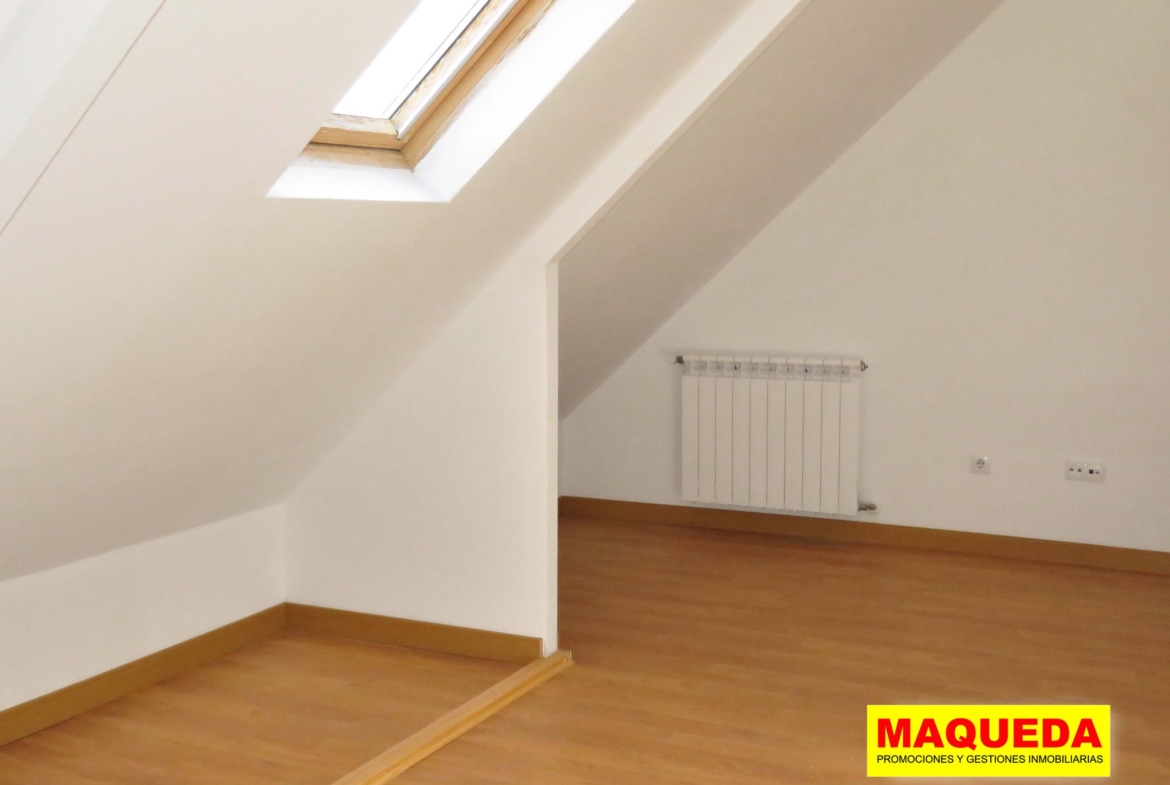 Dormitorio en planta ático con suelo de tarima, techos abuhardillados y ventanas de velux