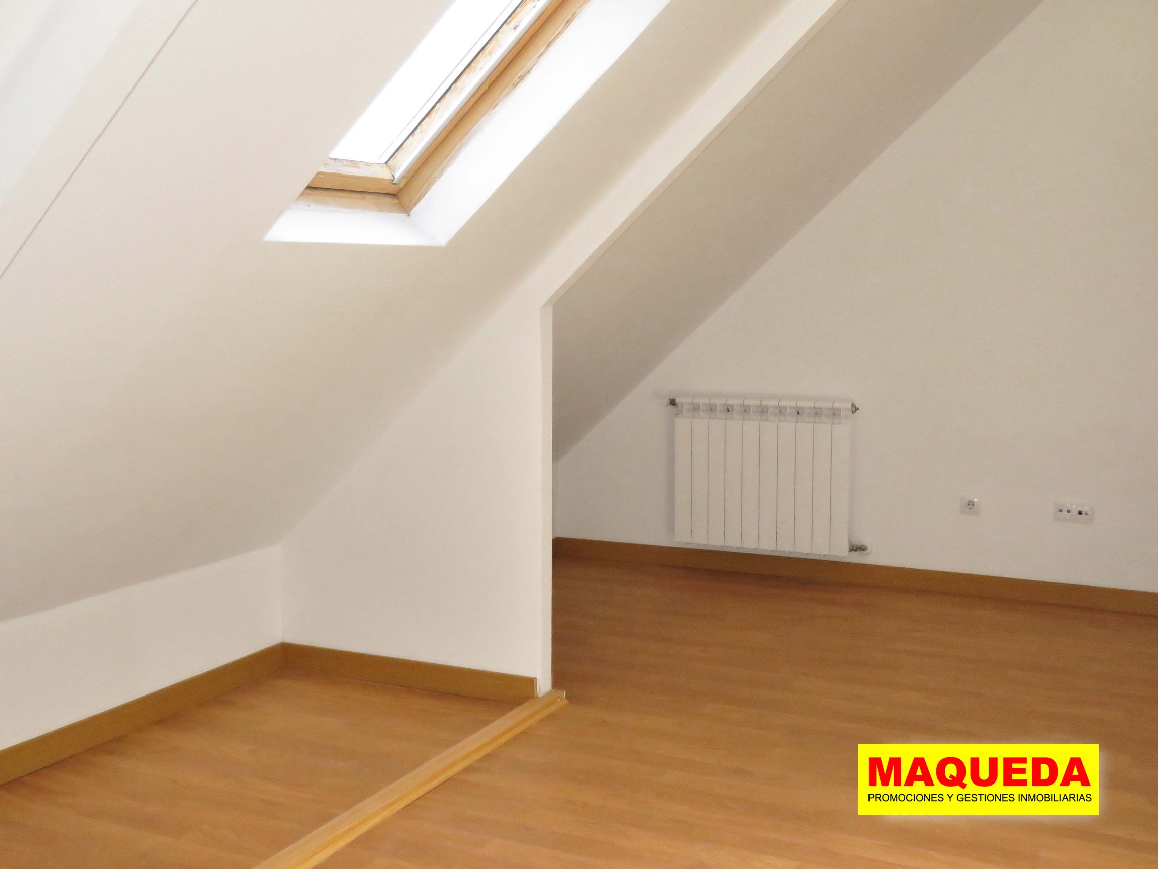 Dormitorio en planta ático con suelo de tarima, techos abuhardillados y ventanas de velux