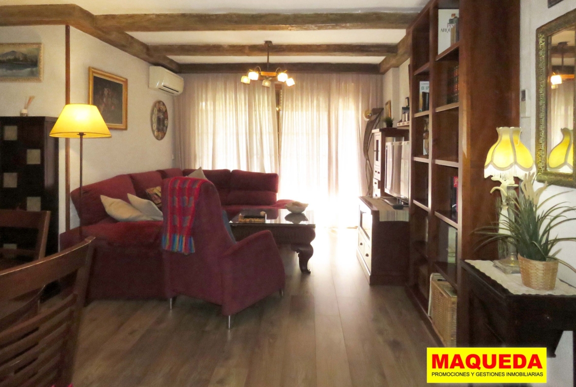 Salón con muebles, vigas y suelos de madera, con puerta de la terraza al fondo