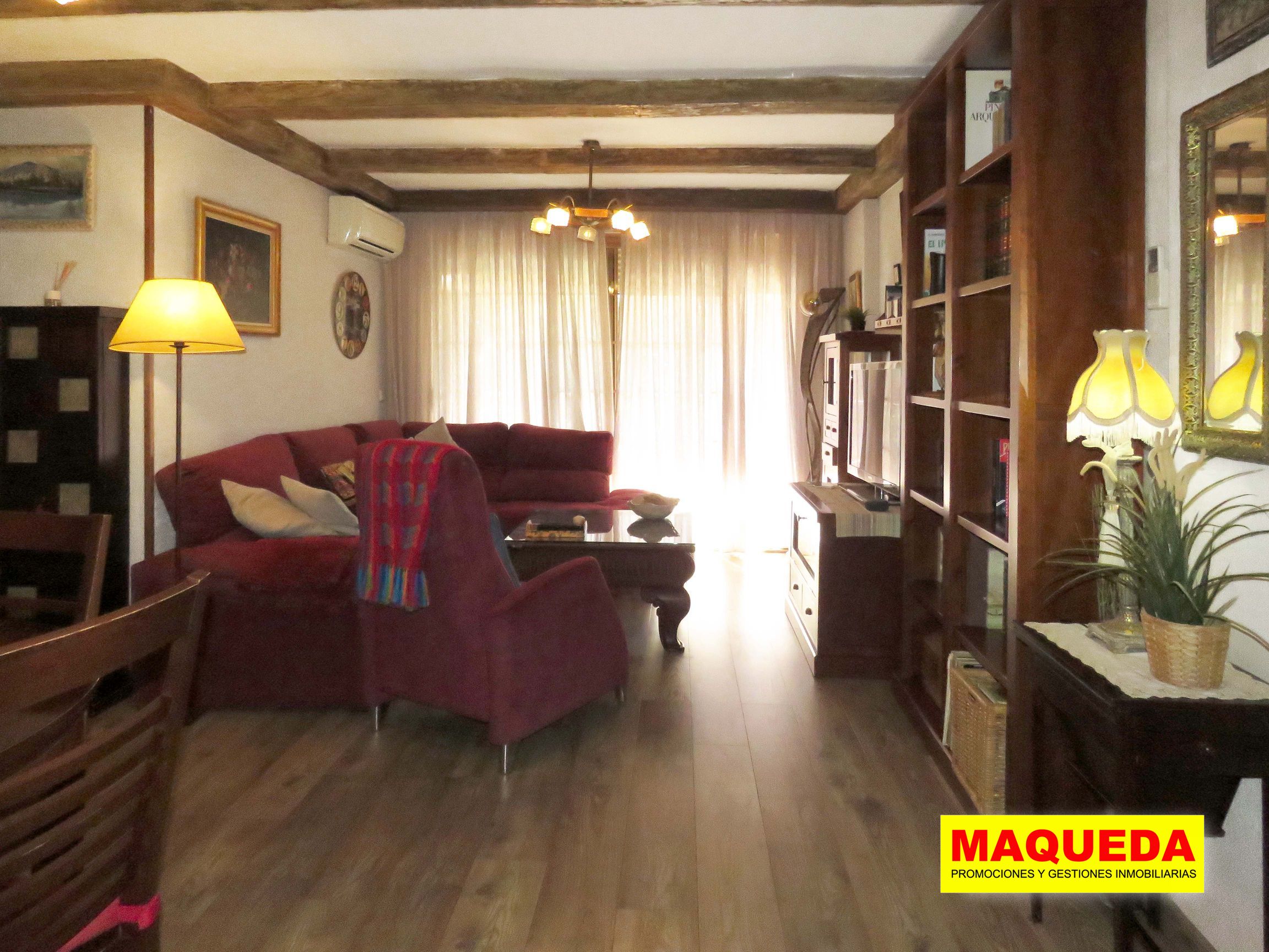 Salón con muebles, vigas y suelos de madera, con puerta de la terraza al fondo