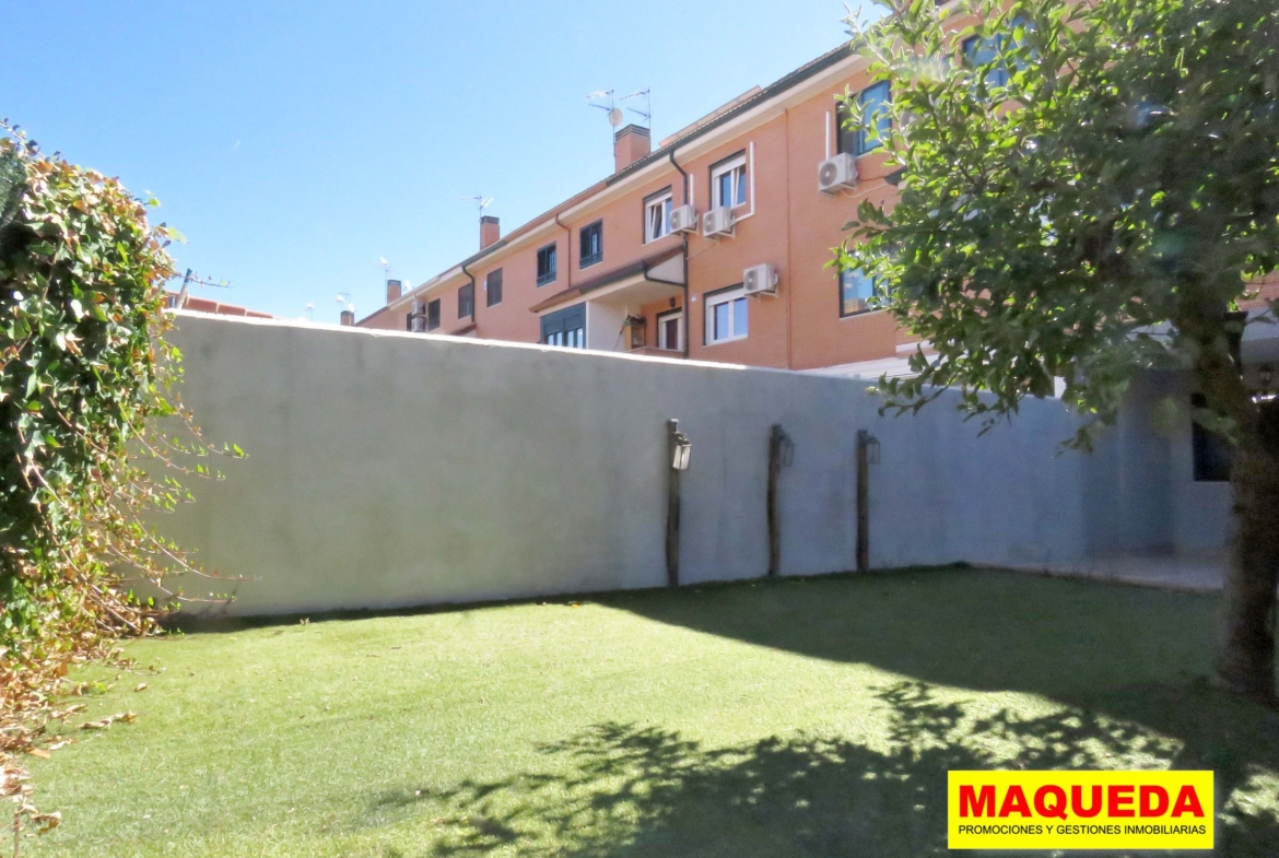 Zona del jardín con césped artificial. Al fondo muro de separación con luminaria decorativa