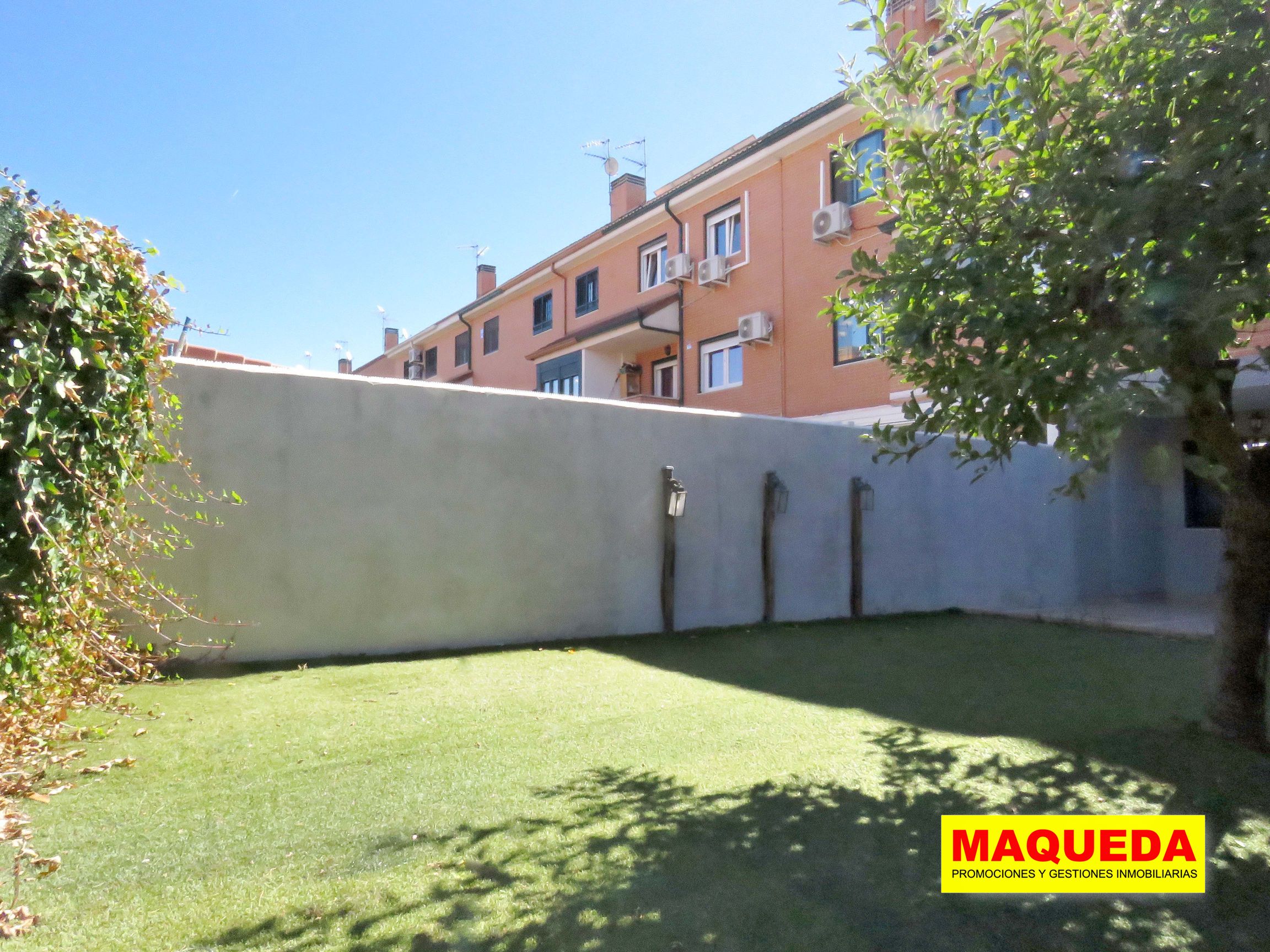 Zona del jardín con césped artificial. Al fondo muro de separación con luminaria decorativa