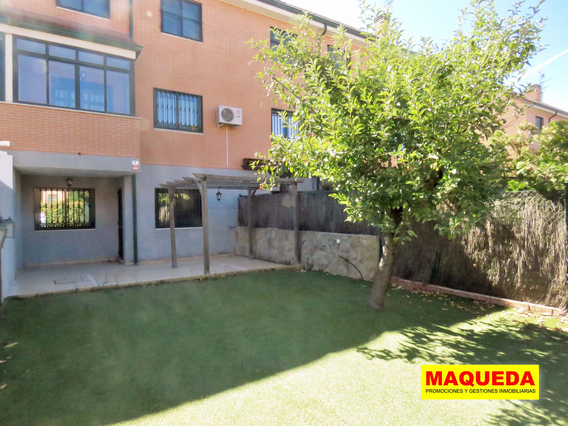 Detalle del jardín con fachada de la casa y árbol frutal sobre césped artificial