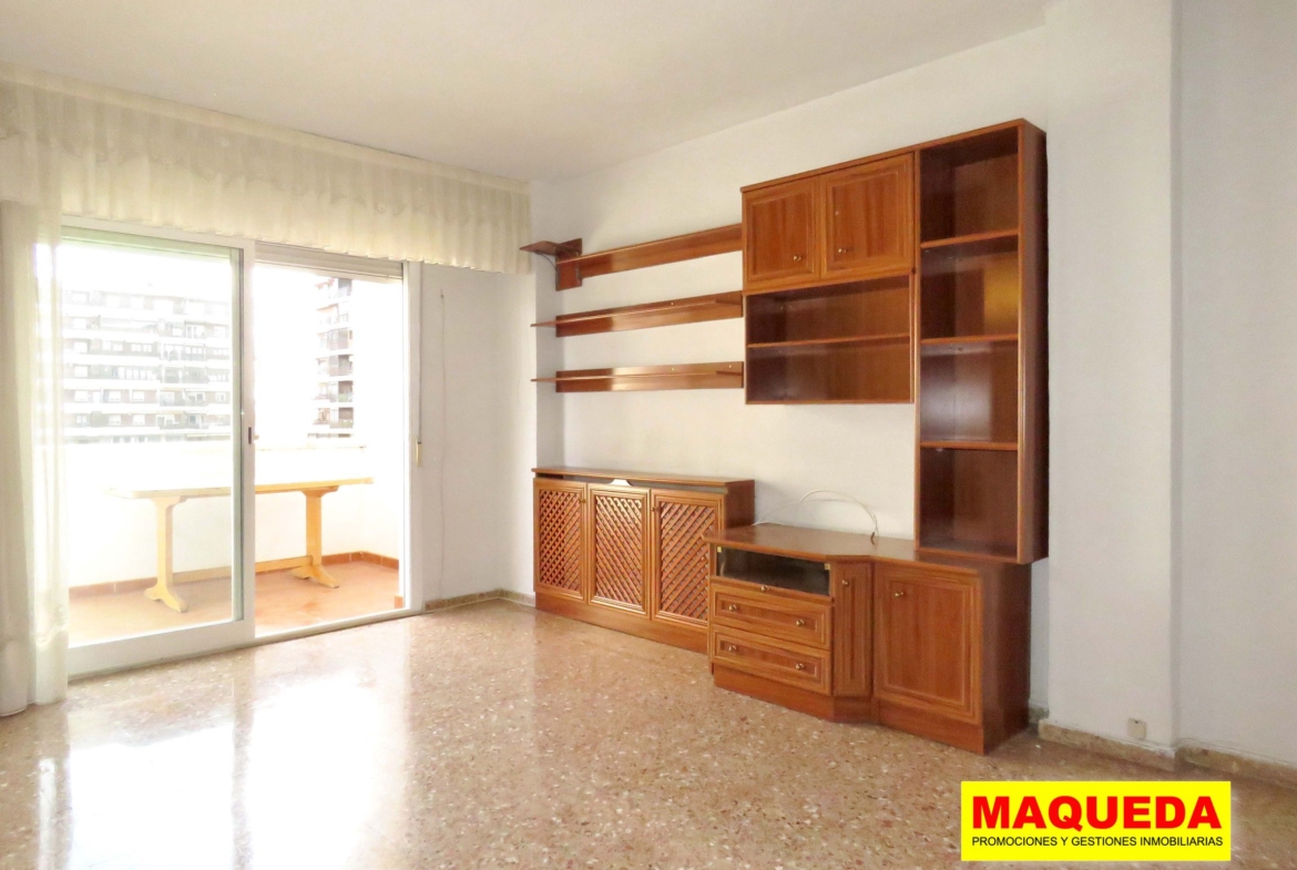 Mueble con estanterías en el salón comedor. A la izquierda puerta de acceso a la terraza con mesa. Al fondo edificios