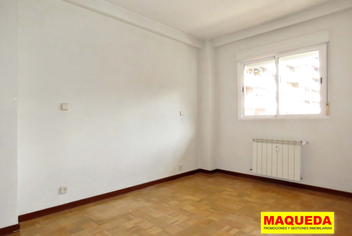 Dormitorio doble con suelos de parquet y radiador bajo ventana