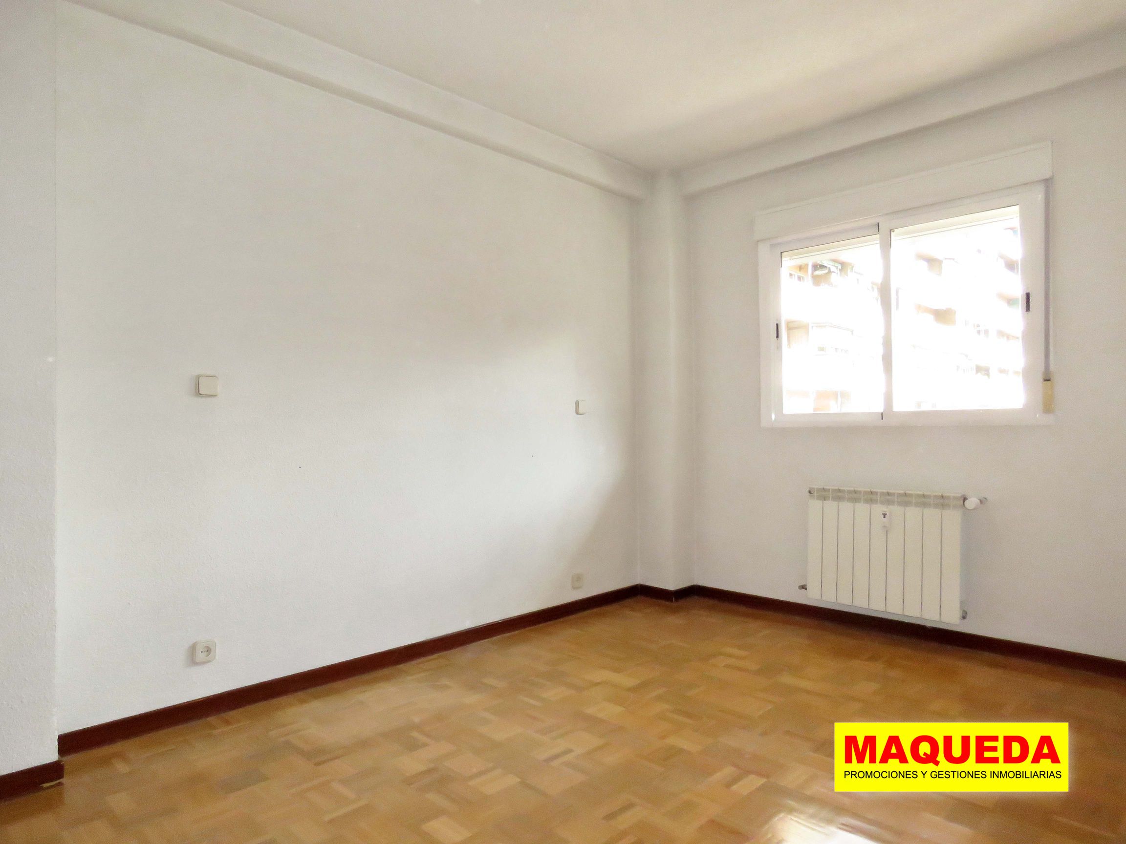 Dormitorio doble con suelos de parquet y radiador bajo ventana